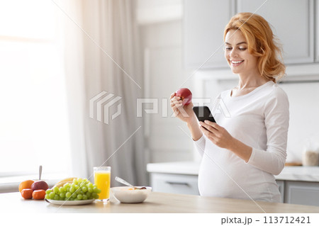 Pregnant woman checking phone with fruit in her hand Pregnant woman checking phone with fruit in her hand 113712421