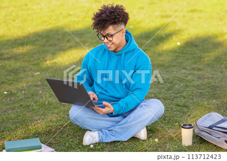 Male student working on laptop in grassy field Male student working on laptop in grassy field 113712423