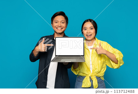 Happy Asian couple pointing at a laptop screen with a blank display Happy Asian couple pointing at a laptop screen with a blank display 113712488