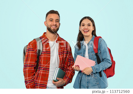 Cheerful couple poses casually with backpacks and textbooks in studio Cheerful couple poses casually with backpacks and textbooks in studio 113712560