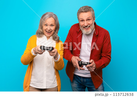 Happy senior couple in casual playing videogames over blue background 113712638