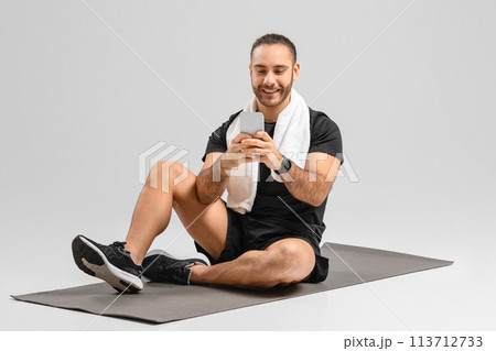 Man using smartphone sitting on fitness mat Man using smartphone sitting on fitness mat 113712733