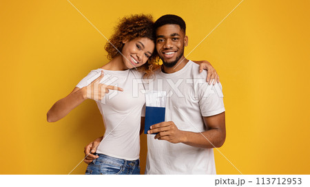 Happy couple showing passports and pointing on yellow background 113712953