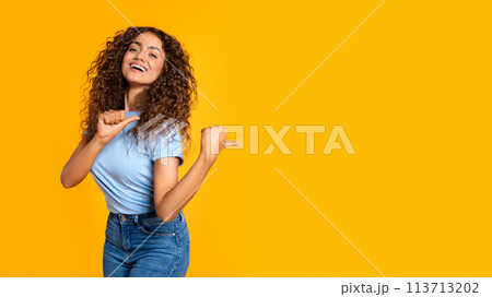 Joyful woman pointing aside with thumb on yellow 113713202