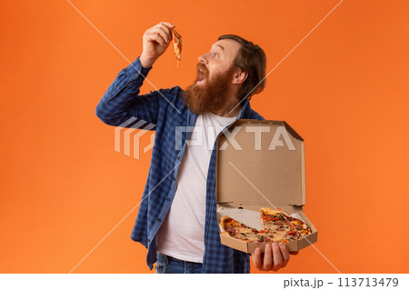 Redhaired bearded man in casual attire eats juicy pizza, studio 113713479