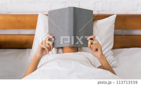 Woman reading book and covering face, lying in bed Woman reading book and covering face, lying in bed 113713539