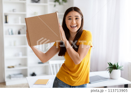 Ecstatic asian woman holding up cardboard box with joyful expression 113713905