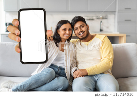 Indian Man and Woman Sitting on Couch Holding Up Blank Cell Phone Indian Man and Woman Sitting on Couch Holding Up Blank Cell Phone 113714010