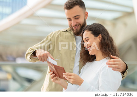 Cheerful couple looking at travel documents while waiting in bright airport terminal Cheerful couple looking at travel documents while waiting in bright airport terminal 113714036