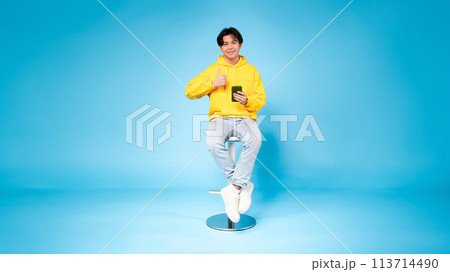 Cheerful young guy with phone gives thumbs up Cheerful young guy with phone gives thumbs up 113714490