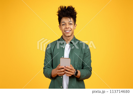 Smiling young black man with phone on yellow Smiling young black man with phone on yellow 113714680