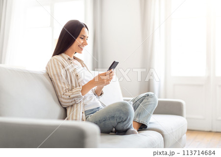 Smiling woman holding phone on sofa at home 113714684