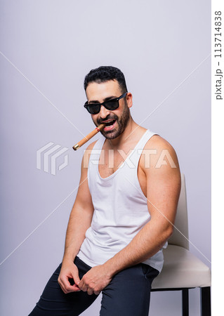 Young man with beard smoking a cigar in studio Young man with beard smoking a cigar in studio 113714838