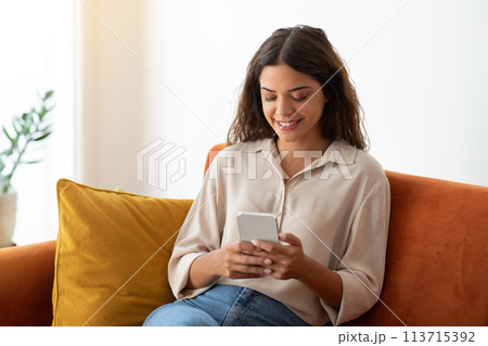Cheerful young woman browsing social media on her smartphone at home 113715392