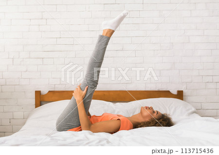 Woman doing yoga exercise on bed at home Woman doing yoga exercise on bed at home 113715436