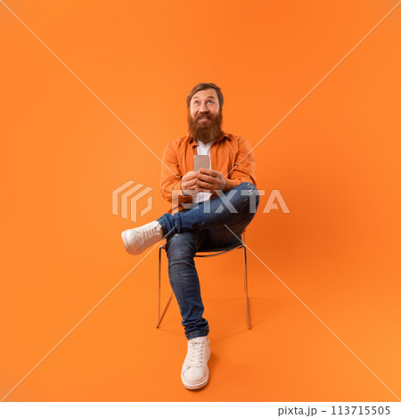 Square shot of redhaired bearded guy browsing on his phone 113715505