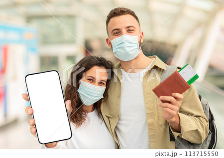 Couple Wearing Masks Holding Passports And Blank Smartphone At Airport Couple Wearing Masks Holding Passports And Blank Smartphone At Airport 113715550