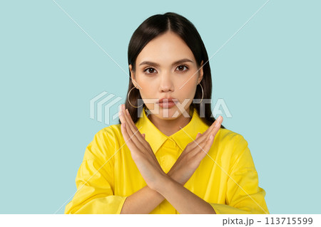 Determined serious beautiful young brunette woman showing crossed hands at camera, blue studio background Determined serious beautiful young brunette woman showing crossed hands at camera, blue studio background 113715599