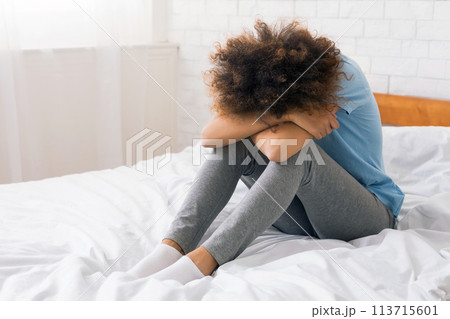 African-american woman suffering from depression sitting on bed 113715601