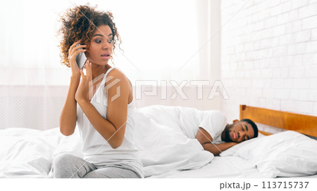 Woman on phone with man asleep in bed 113715737