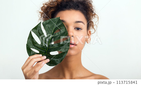 Woman with tropical leaf covering half of face Woman with tropical leaf covering half of face 113715841