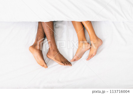 Loving couple legs lying on bed under blanket Loving couple legs lying on bed under blanket 113716004