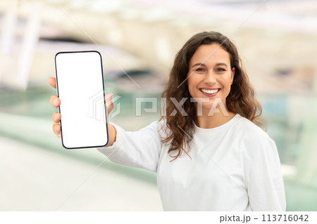 Happy Young Woman Standing In Airport And Showing Big Blank Smartphone Happy Young Woman Standing In Airport And Showing Big Blank Smartphone 113716042