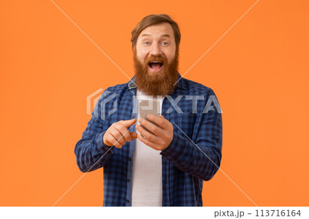 Red haired businessman expresses surprise using app on smartphone, studio Red haired businessman expresses surprise using app on smartphone, studio 113716164