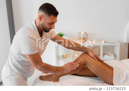Masseur applying pressure to African American woman's leg 113716225