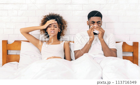 Sick african-american couple blowing noses in bed Sick african-american couple blowing noses in bed 113716349