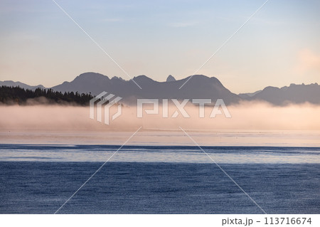Misty lake framed by mountains, creating a serene natural landscape Misty lake framed by mountains, creating a serene natural landscape 113716674