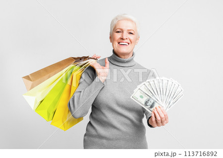 Elderly woman with money and bags on grey background Elderly woman with money and bags on grey background 113716892