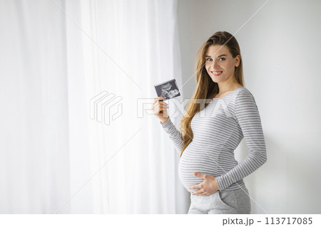 Expectant woman holding ultrasound photo, home interior 113717085