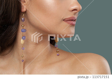 Gold earring with blue and purple chalcedony stones on jewelry model closeup. 113717151