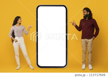 Man and woman pointing at blank phone screen on yellow 113717609
