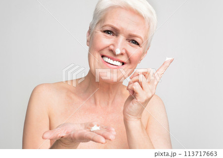 Senior woman presenting skin cream on grey background 113717663