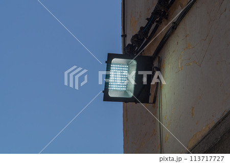 An LED lantern mounted on the street wall dimly illuminates the wall during dusk on dark blue sky background. The interval of time of day that is observed by a change in the degree of illumination An LED lantern mounted on the street wall dimly illuminates the wall during dusk on dark blue sky background. The interval of time of day that is observed by a change in the degree of illumination 113717727
