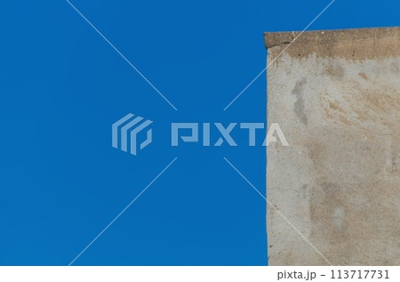 A small section of the edge of a blurred building wall with rough uneven plaster against a blue clear sky. Blank for artwork, mockup 113717731