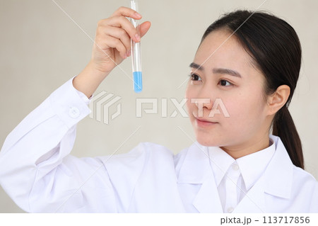 試験管を真剣な表情で見つめる白衣の女性 113717856