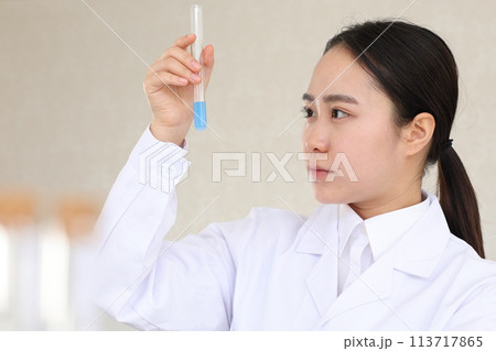 試験管を真剣な表情で見つめる白衣の女性 113717865