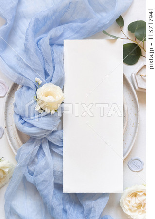 Card near blue tulle fabric knot and cream roses on plates top view copy space, wedding mockup 113717941