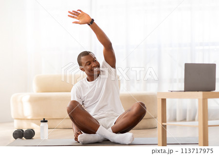 Man stretching arm during home workout with laptop 113717975