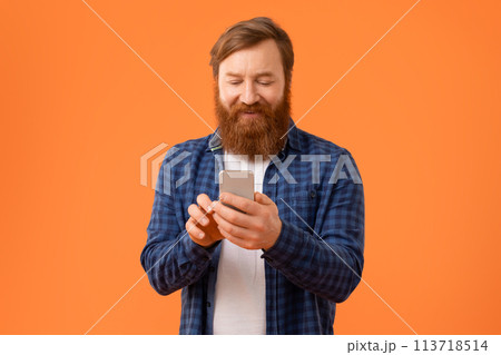 redhaired guy smiles while browsing on cell phone in studio redhaired guy smiles while browsing on cell phone in studio 113718514