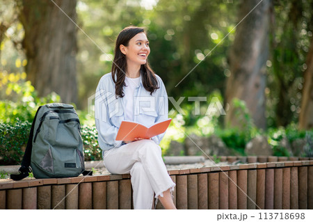 Student reading book while sitting on a bench in park 113718698