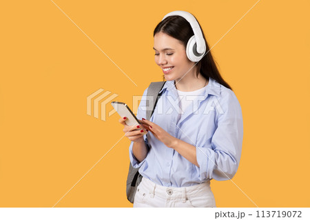 Woman focused on smartphone with headphones, yellow background 113719072