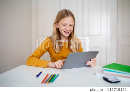 Cheeful Teen Girl Sitting at Table With Tablet Cheeful Teen Girl Sitting at Table With Tablet 113719122