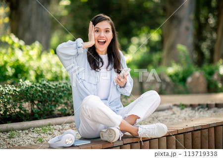 Excited woman posing with smartphone, touching her head 113719338