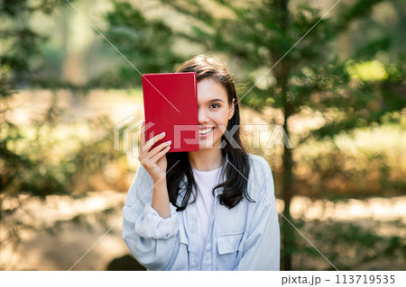 Woman holding red book covering half her face 113719535