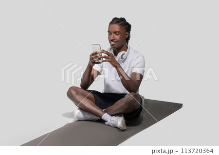 Man texting on phone while sitting on mat 113720364