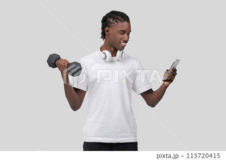 Man with dumbbell browsing smartphone on white background 113720415